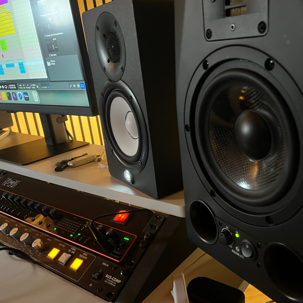 Dettaglio dei monitor da studio sulla scrivania di Sthage, con lo schermo del software di produzione e un compressore a rack